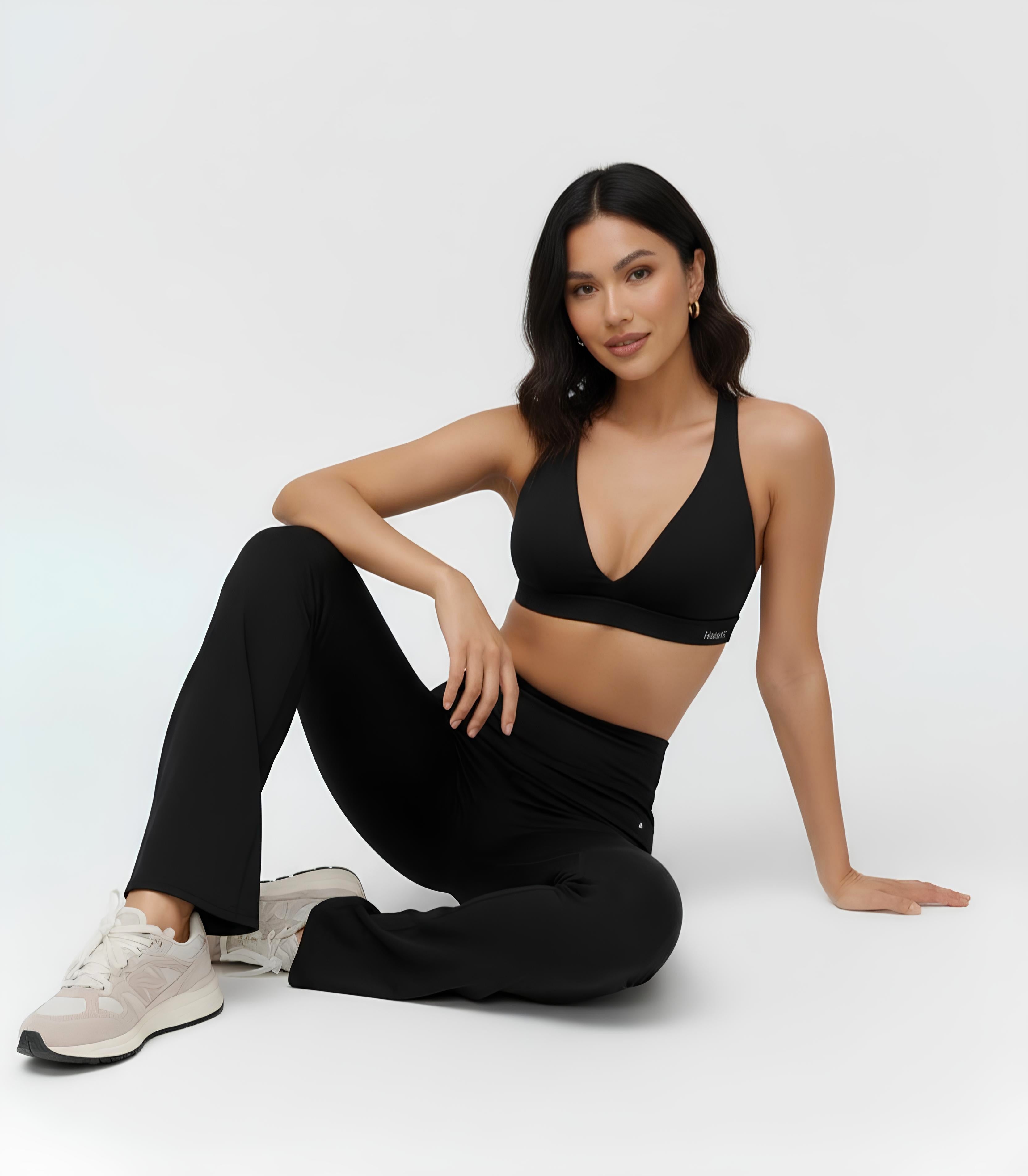 Woman wearing a black sports bra and leggings sitting on a white background